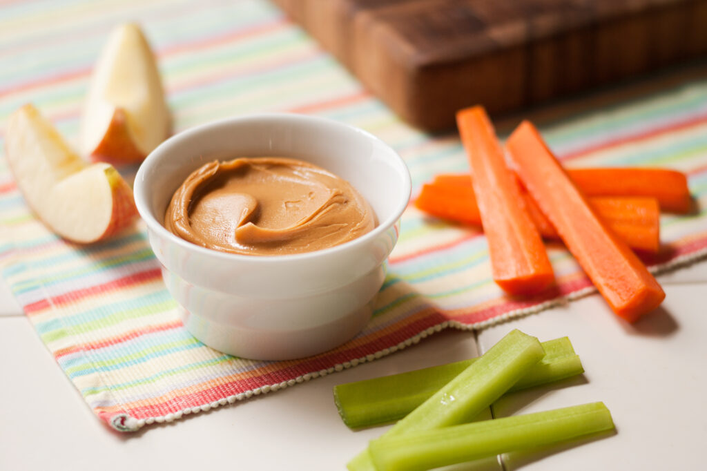 Peanut butter served in a bowl with celery, apples and carrots to dip.